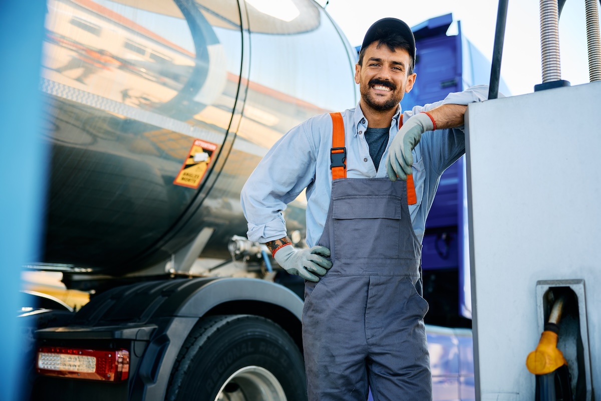 man wearing service overalls and gloves, smiling next to guel tank